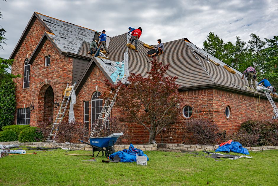 Roofing crew working on the pitched roof of a brick home