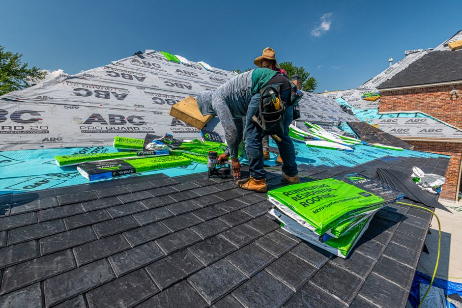 Roofers installing a slate roof on the side of a brick house